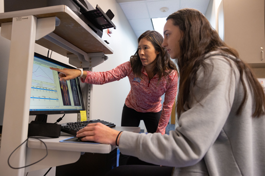 Photograph of an instructor pointing at a computer screen while working with a student.